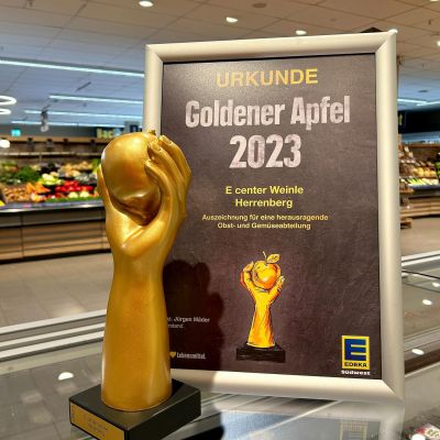 Plakat zum Gewinn des Goldenen Apfels durch das e-Center Weinle, Herrenberg mit dem "Pokal" des goldenen Apfels gehalten einer goldenen Hand