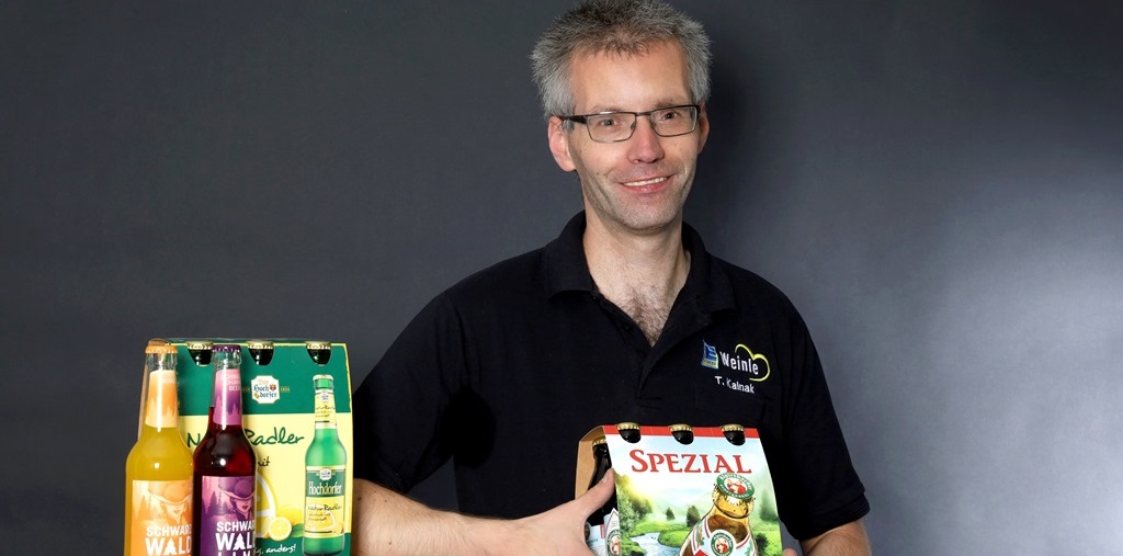 Mitarbeiterfoto im Edeka T-Shirt mit Getränkeflschen im Vordergrund