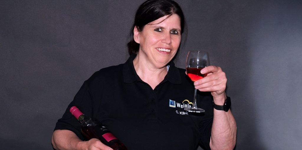 Mitarbeiterin im Edeka T-Shirt mit einer Flasche Wein im Arm und einem Glas Rotwein in der Hand