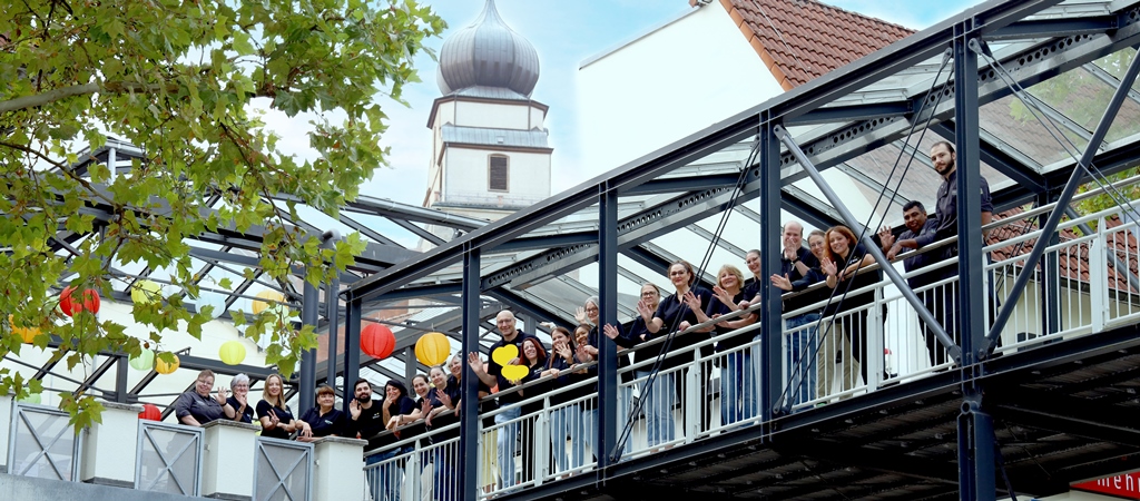 Eine Gruppe von Edeka Weinle Mitarbeitern winkt von einer Fußgängerbrücke